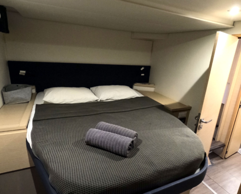 Cabin with made bed, towel, and side cabinetry.